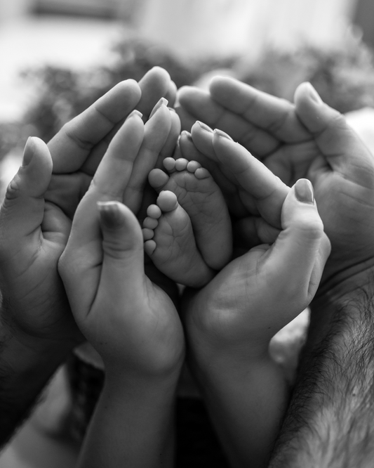 Black and white photo of fathers hands cupping mothers hands cupping babies newborn feet